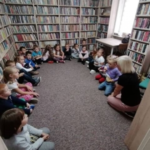 Dzieci siedzą w okręgu, słuchają zagadek zadawanych orzez panią bibliotekarkę